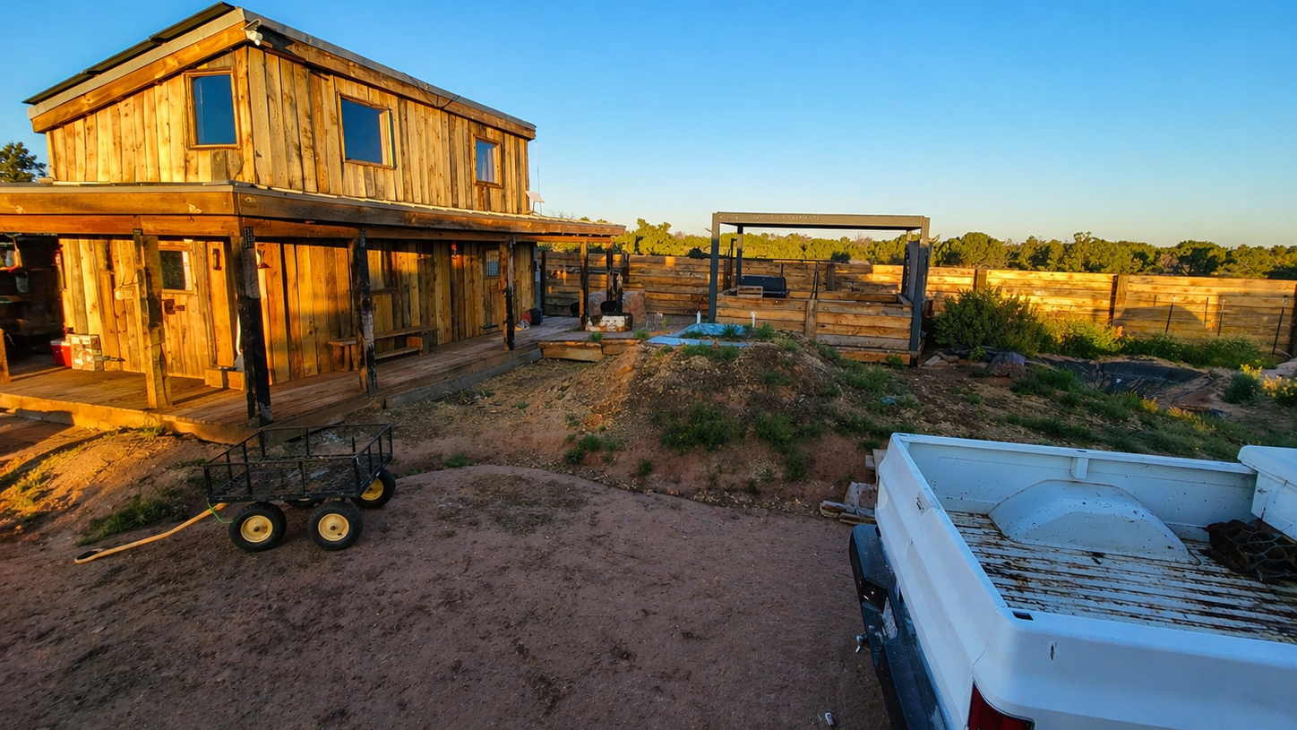 Off-grid homestead showing cabin, water system area, and in-progress layout during early morning build stage